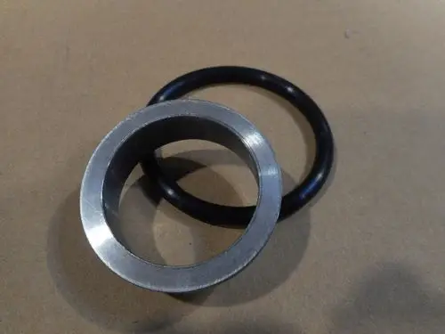 Schwarze O-Ring-Dichtung und metallene Durchführung, dargestellt auf einer neutralen Oberfläche, möglicherweise für Remeha-Anwendungen.
